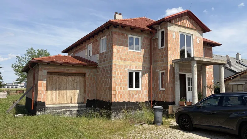 Rohbau eines Einfamilienhauses mit Ziegelwänden und Dachkonstruktion unter blauem Himmel.