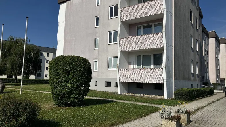 Mehrfamilienhaus mit gepflegter Grünfläche und Balkonen unter blauem Himmel.