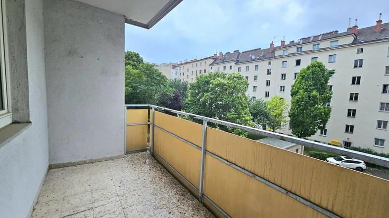 Geräumiger Balkon mit Fliesenboden und Blick auf die umliegenden Gebäude und Bäume.