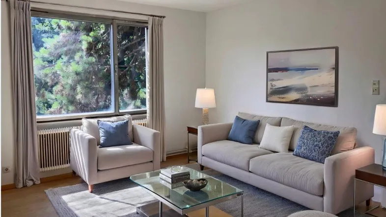 Helles, virtuell inszeniertes Wohnzimmer mit beigem Sofa, Teppich und Blick ins Grüne.