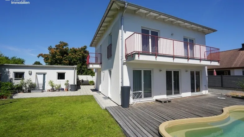 Weißes Einfamilienhaus mit Balkonen, Holzterrasse und einem kleinen Pool im Garten.