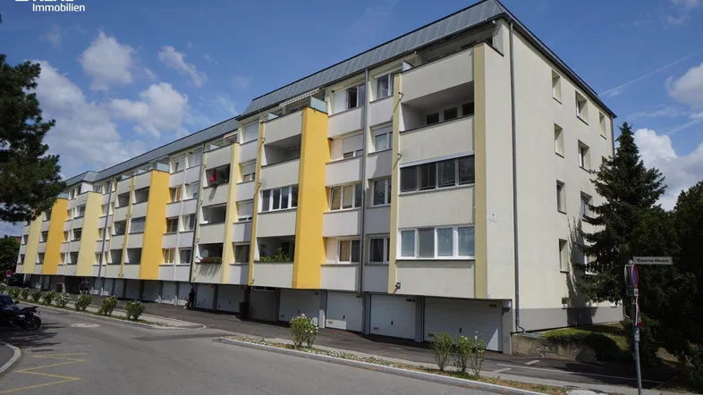 Mehrstöckiges Wohngebäude mit gelben Akzenten, Balkonen und Garagen entlang einer Straße.