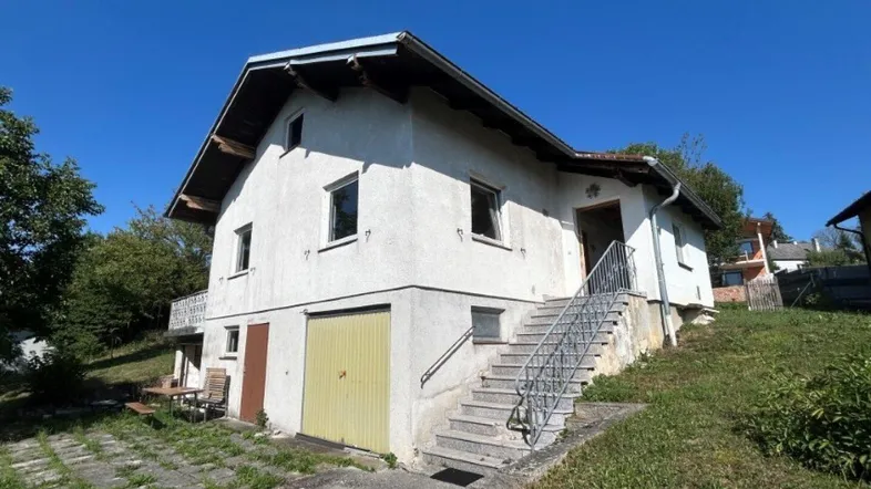 Freistehendes Haus mit Garage im Untergeschoss und Außentreppe zum Eingang.