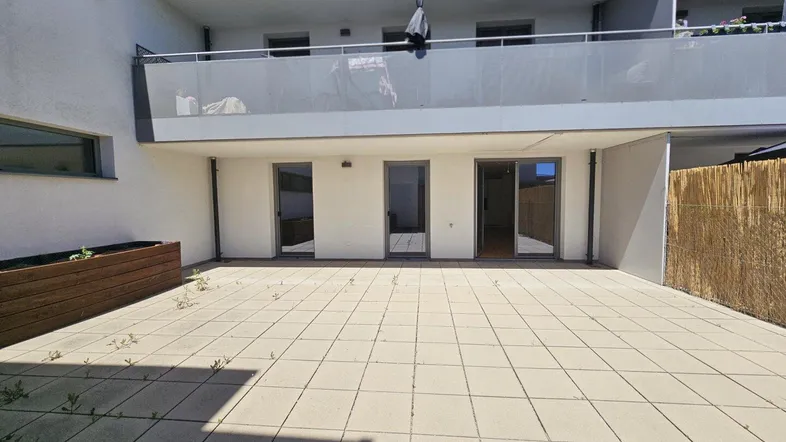 Große gepflasterte Terrasse mit Zugang zu den Innenräumen und einem Balkon darüber.