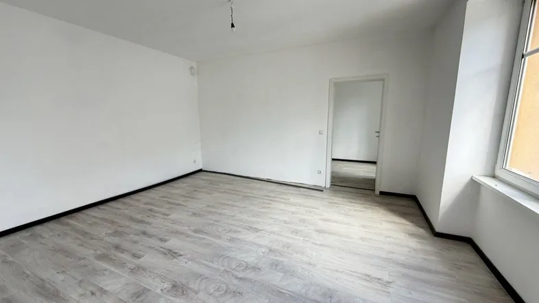 Helles, leeres Zimmer mit modernem Laminatboden und weißen Wänden, bereit für die individuelle Gestaltung.