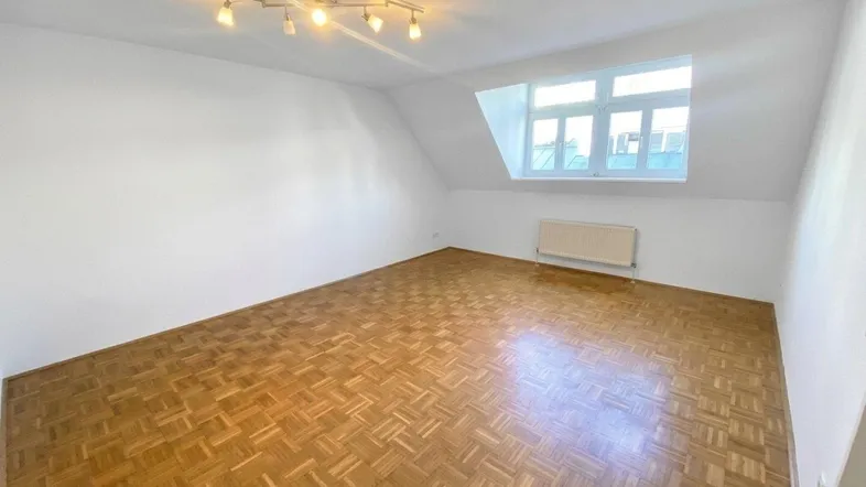 Helles Zimmer im Dachgeschoss mit Parkettboden und schrägen Wänden, ideal als Schlafzimmer.