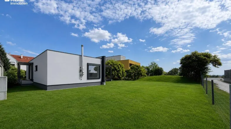 Moderner Neubau mit großem, gepflegtem Rasen und klarem Himmel an einem sonnigen Tag.