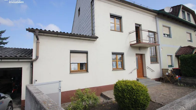 Vorderansicht des Hauses mit kleiner Gartenfläche, Balkon und Garagenzufahrt.
