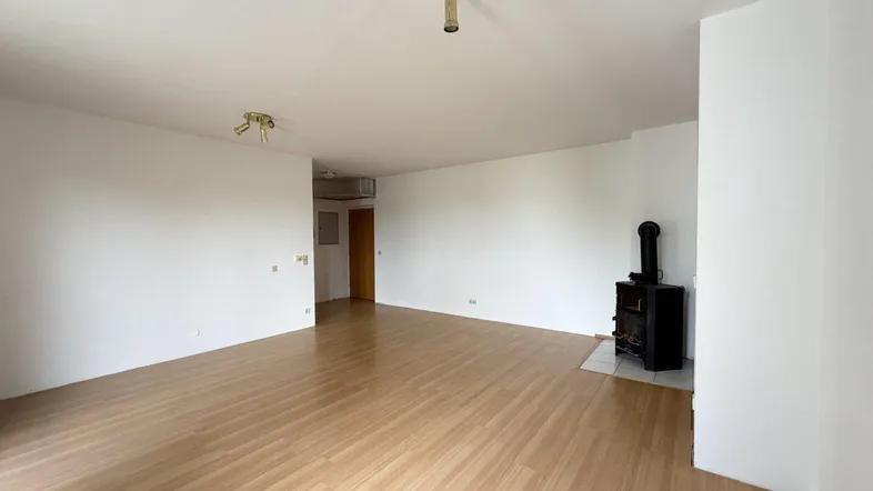 Geräumiges Wohnzimmer mit hellem Holzboden und einem gemütlichen Holzofen, bereit zur individuellen Gestaltung.
