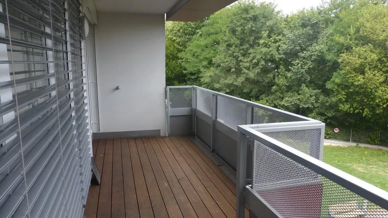 Geräumiger Balkon mit Holzboden und Metallgeländer, umgeben von viel Grün.