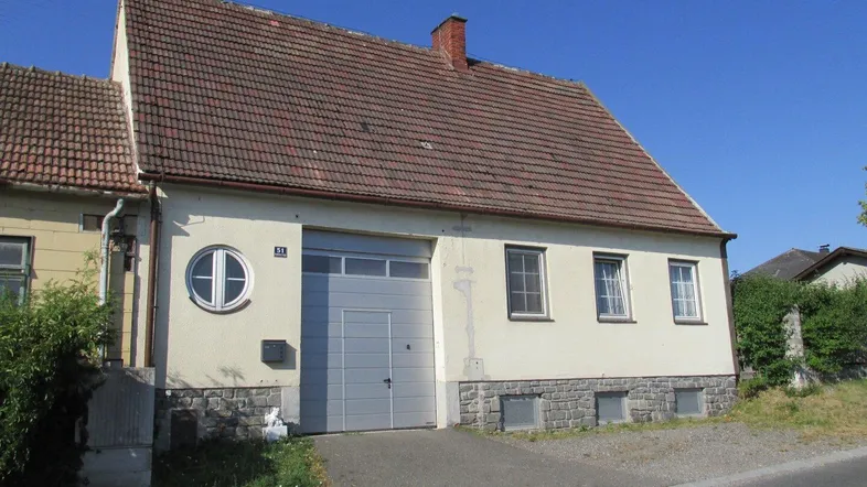 Vorderansicht eines Einfamilienhauses mit Garagentor und Satteldach unter blauem Himmel.