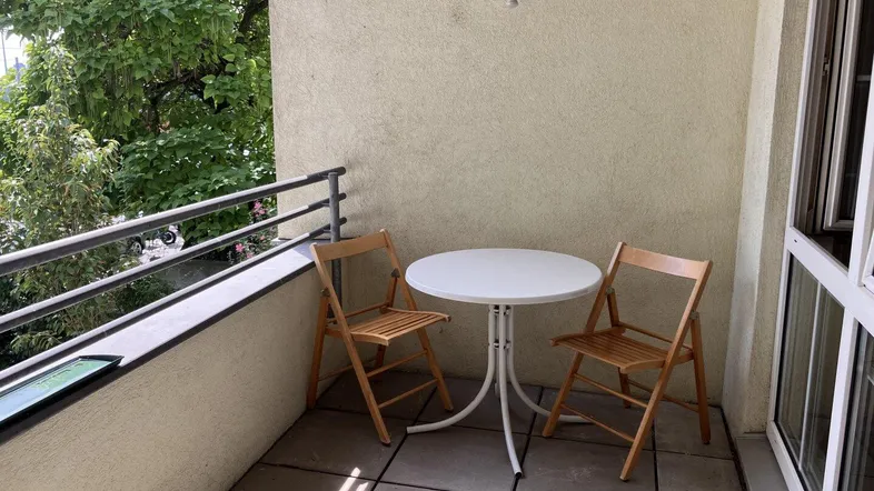Möblierter Balkon mit kleinem Tisch und Stühlen, umgeben von grünen Bäumen für entspannte Stunden.