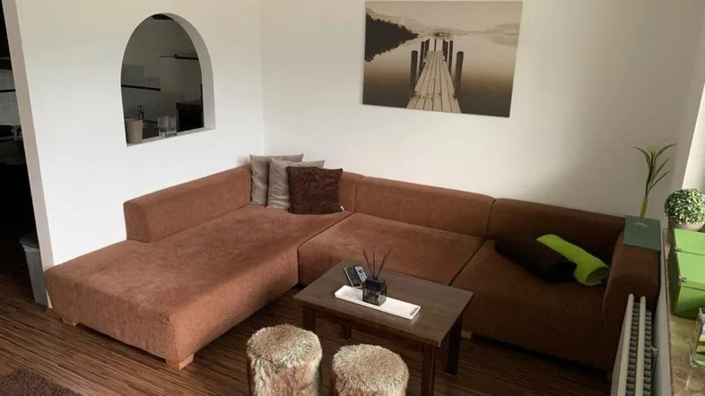 Gemütliches Wohnzimmer mit braunem Ecksofa, Holzboden und dekorativem Wandbild.