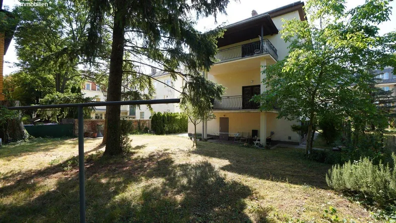Mehrstöckiges Gebäude mit Balkonen und einem weitläufigen Gartenbereich im Vordergrund.