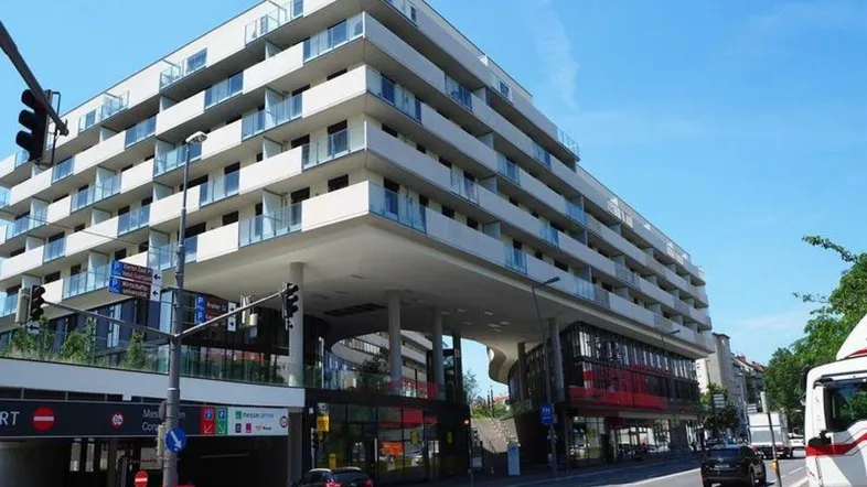 Modernes Mehrfamilienhaus mit zahlreichen Balkonen und einer Tiefgaragenzufahrt an einer belebten Straße.