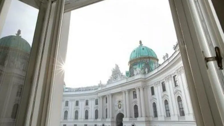Blick aus einem geöffneten Fenster auf ein prächtiges historisches Gebäude mit einer markanten grünen Kuppel.