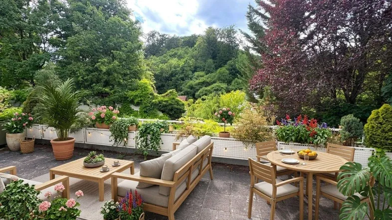 Große, möblierte Terrasse mit Ess- und Loungebereich, umgeben von üppigem Grün und Pflanzen.