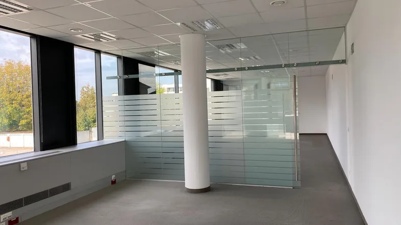 Geräumiges Büro mit großen Fenstern, Teppichboden und modernen Glaswänden für flexible Raumgestaltung.