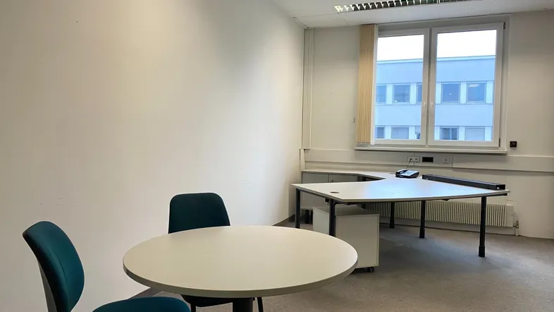 Helles Büro mit Teppichboden, Schreibtisch und Besprechungstisch, ideal für produktives Arbeiten.