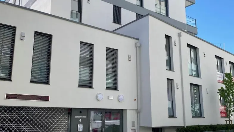 Modernes Mehrfamilienhaus mit weißer Fassade, grauen Akzenten und großen Fenstern unter blauem Himmel.