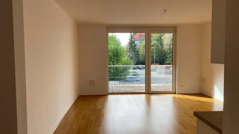 Helles Wohnzimmer mit Parkettboden und Zugang zu einem Balkon, bietet viel Tageslicht.