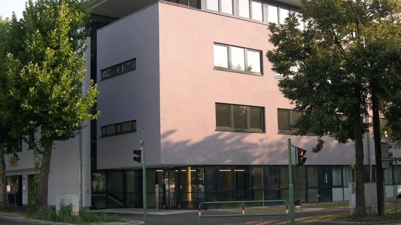 Modernes Bürogebäude mit großen Fenstern und einer schlichten, hellgrauen Fassade an einer Straßenecke.