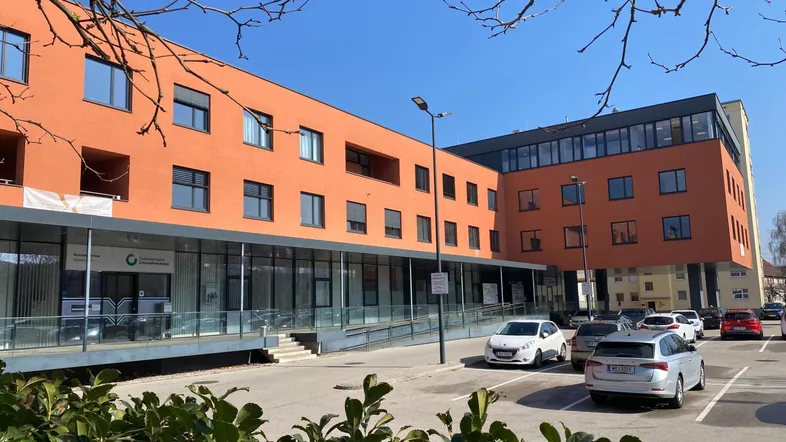 Modernes Bürogebäude mit orangefarbener Fassade und großem Parkplatz unter blauem Himmel.