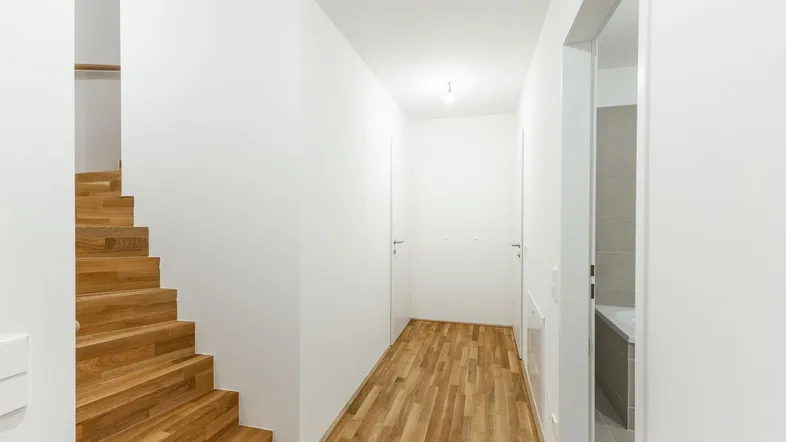 Heller Flur mit Holztreppe und Parkettboden, der zu weiteren Räumen führt.
