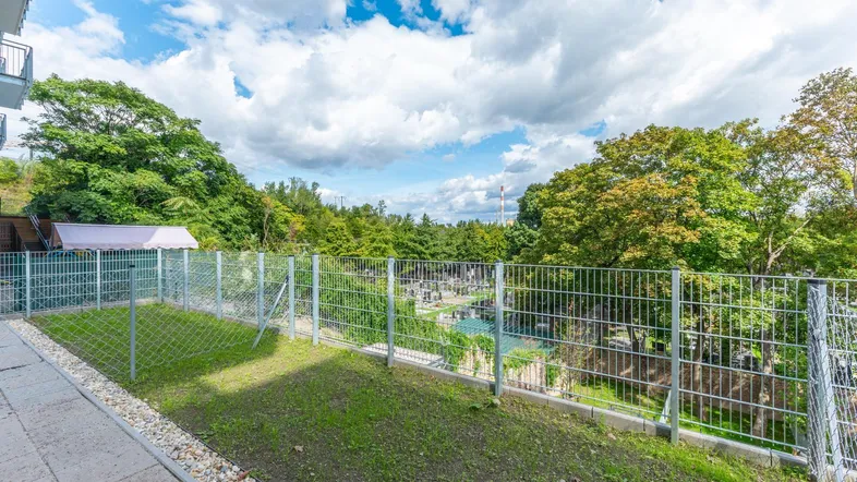 Kleiner privater Gartenbereich mit Rasenfläche und Blick ins Grüne, umzäunt von einem Metallzaun.