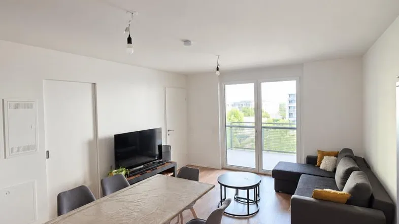 Heller Wohn- und Essbereich mit modernem Sofa, Esstisch und Zugang zu einem Balkon.