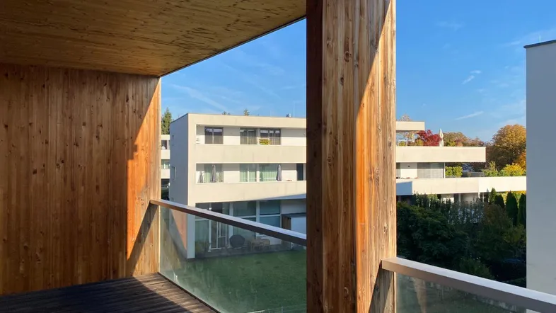Geräumiger Balkon mit Holzverkleidung und Blick auf moderne Gebäude und grüne Umgebung.
