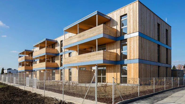Modernes Mehrfamilienhaus mit Holzfassade und blauen Akzenten unter klarem Himmel.