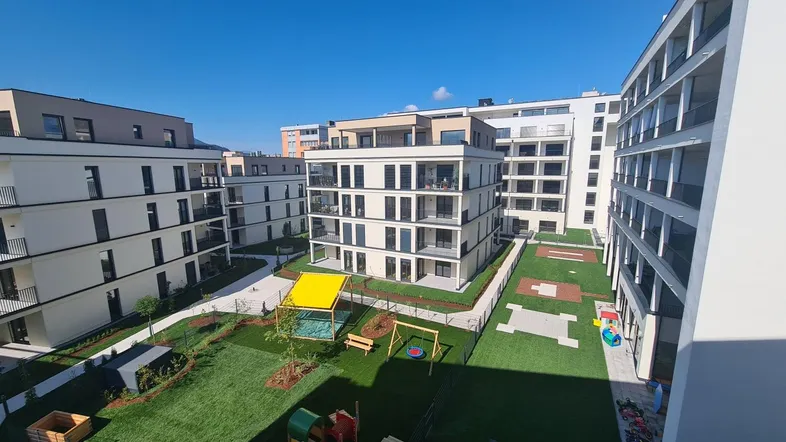 Moderner Wohnkomplex mit mehreren Gebäuden und einem grünen Innenhof mit Spielplatz.