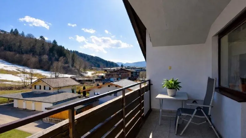 Sonniger Balkon mit Bergblick und Sitzgelegenheit, umgeben von alpiner Landschaft.