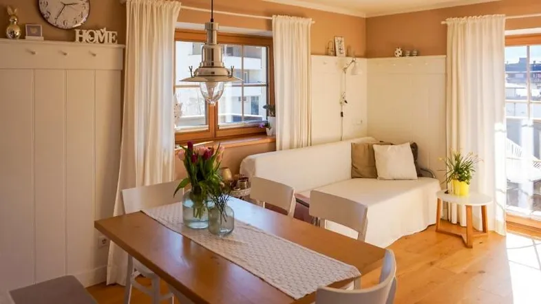 Heller Wohn- und Essbereich mit Holztisch, bequemer Couch und Zugang zum Balkon.