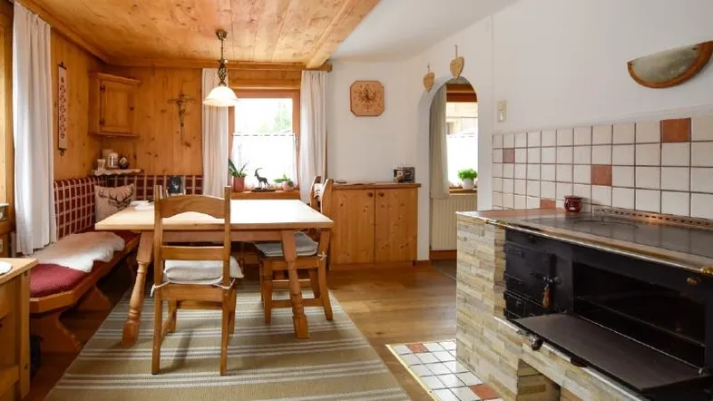 Traditioneller Essbereich mit Holztisch, Eckbank und einem rustikalen Holzofen mit Fliesen. 