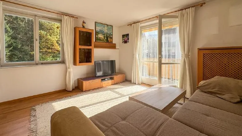 Helles Wohnzimmer mit beigem Sofa, Holzboden und Zugang zu einem Balkon, der viel Sonnenlicht hereinlässt.