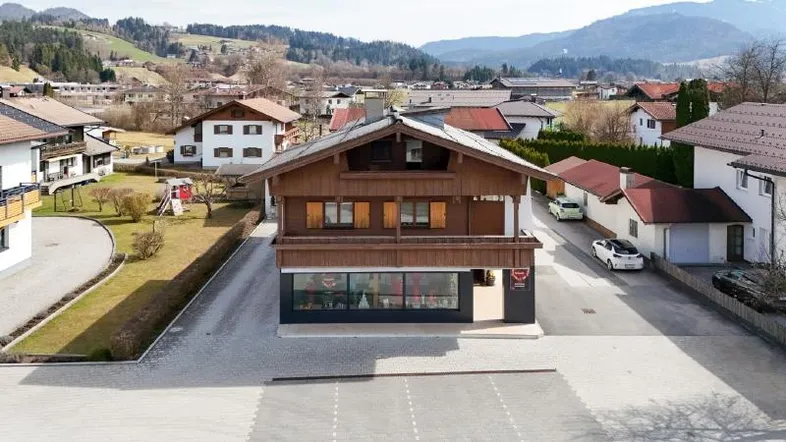 Traditionelles Holzhaus mit Satteldach und Geschäft im Erdgeschoss, umgeben von einer ländlichen Berglandschaft.