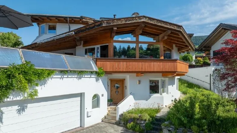 Charmantes Haus im alpinen Stil mit Garage, Holzelementen und Solaranlage unter blauem Himmel.