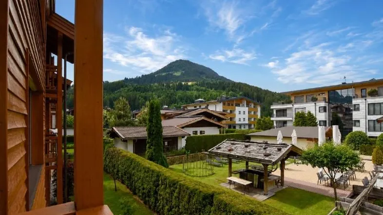 Blick vom Balkon auf den gepflegten Gemeinschaftsgarten mit Grillplatz und Bergsicht.