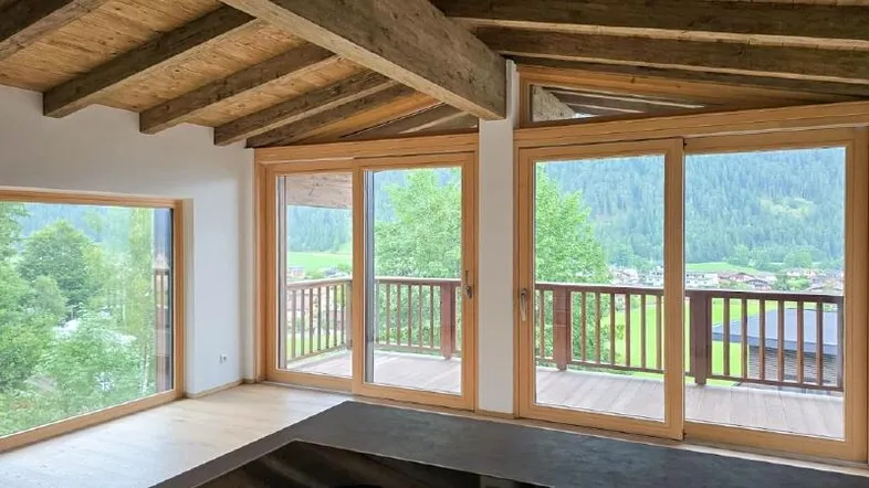 Helles Wohnzimmer mit Holzbalkendecke, großen Fenstern und Zugang zum Balkon mit Bergblick.