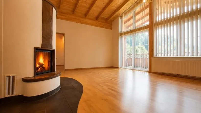 Helles Wohnzimmer mit Kamin, hohen Holzdecken und großen Fenstern, die viel Tageslicht hereinlassen.