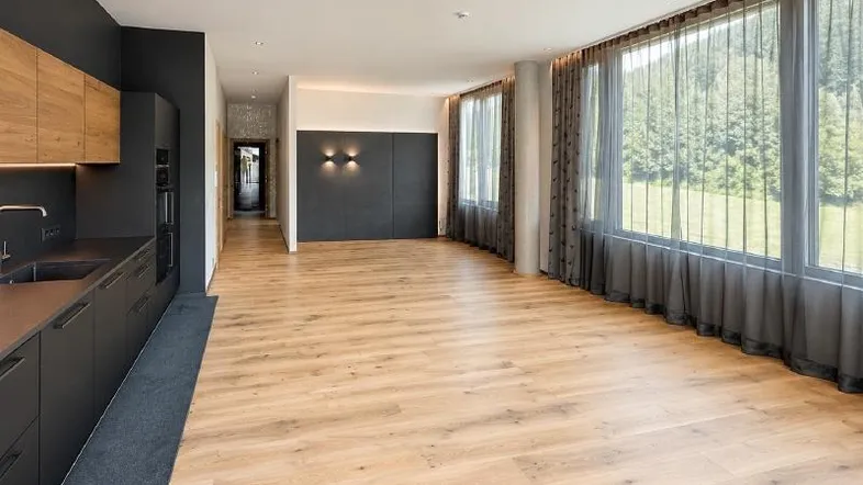 Geräumiger, offener Wohnbereich mit Holzboden, großen Fenstern und Blick ins Grüne.