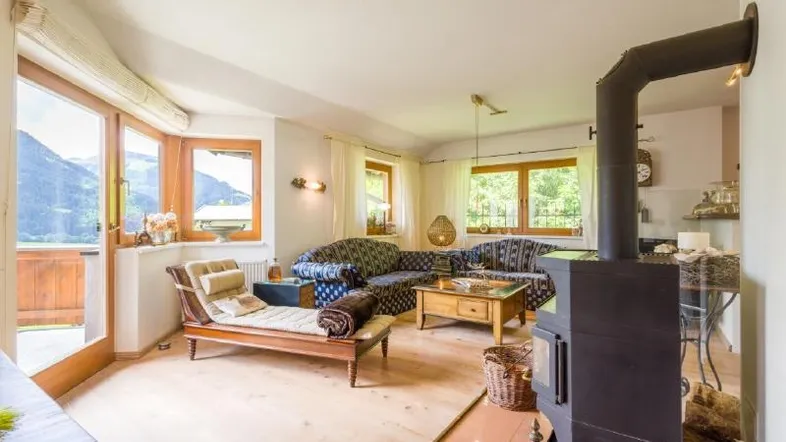Helles Wohnzimmer mit Holzboden, gemütlichem Kaminofen und Zugang zu einem Balkon mit Bergblick.