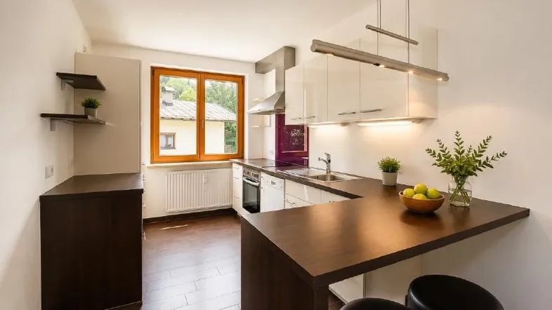 Helle Küche mit modernen weißen Schränken, dunkler Arbeitsplatte und integriertem Essbereich am Fenster.
