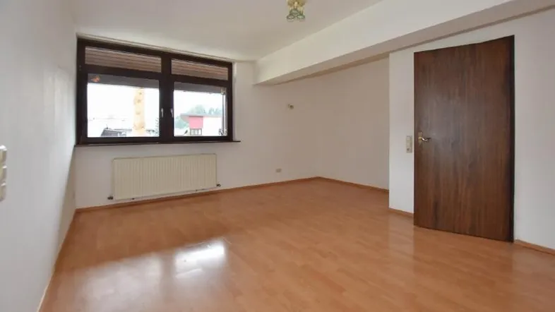 Helles, leeres Zimmer mit Laminatboden und großem Fenster, bereit zur individuellen Gestaltung.
