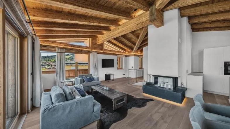 Geräumiges Wohnzimmer mit sichtbaren Holzbalken, Kamin und weitem Blick ins Grüne.