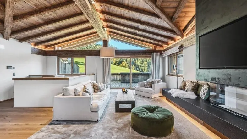 Helles Wohnzimmer mit Holzbalkendecke, Kamin und Zugang zu einem Balkon mit Bergblick.