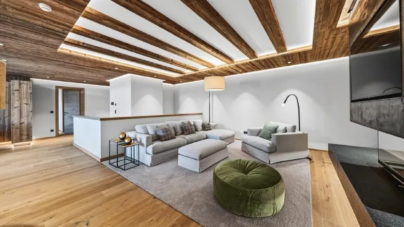 Geräumiges Wohnzimmer mit Holzbalkendecke, modernem Sofa und indirekter Beleuchtung, ideal zum Entspannen.