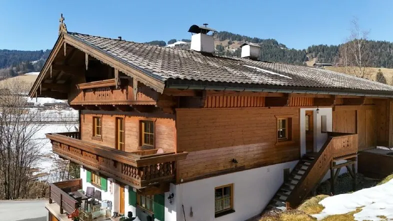 Traditionelles Holzhaus im alpinen Stil mit Balkonen und Satteldach in einer verschneiten Berglandschaft.